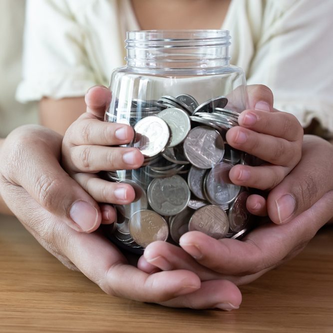 Adult and kid hands holding a coins jar together in savings and donation concept